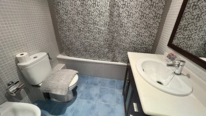 A bathroom with a toilet, bidet, sink, and a shower with mosaic tiles. - Bright Two-Bedroom Apartment in Maragall (Barcelona)