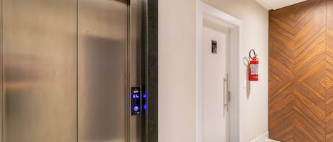 Um elevador com visor digital, extintor fixado na parede e porta com design em painel de madeira.