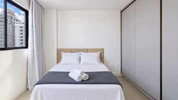 A hotel room with a bed, a window with curtains, and a view of buildings outside.