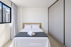 Una habitación de hotel con una cama, un ventanal con cortinas y vistas a edificios.