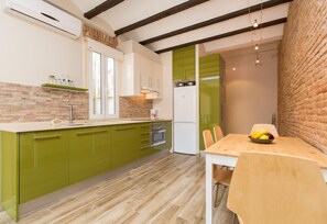 A compact kitchen with green cabinets, a white countertop, and a wooden dining table with chairs. - Urban Charming Gracia  (Barcelona)