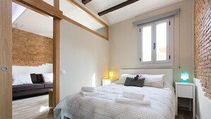 Ein modernes Schlafzimmer mit Bett, Nachttischen, einem Fenster und einem Sofa im angrenzenden Raum.