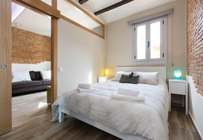 Quarto moderno com cama, mesas de cabeceira, uma janela e um sofá na sala adjacente.