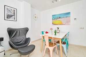 Un coin repas avec une table blanche, des chaises colorées, une chaise noire et un tableau accroché au mur.