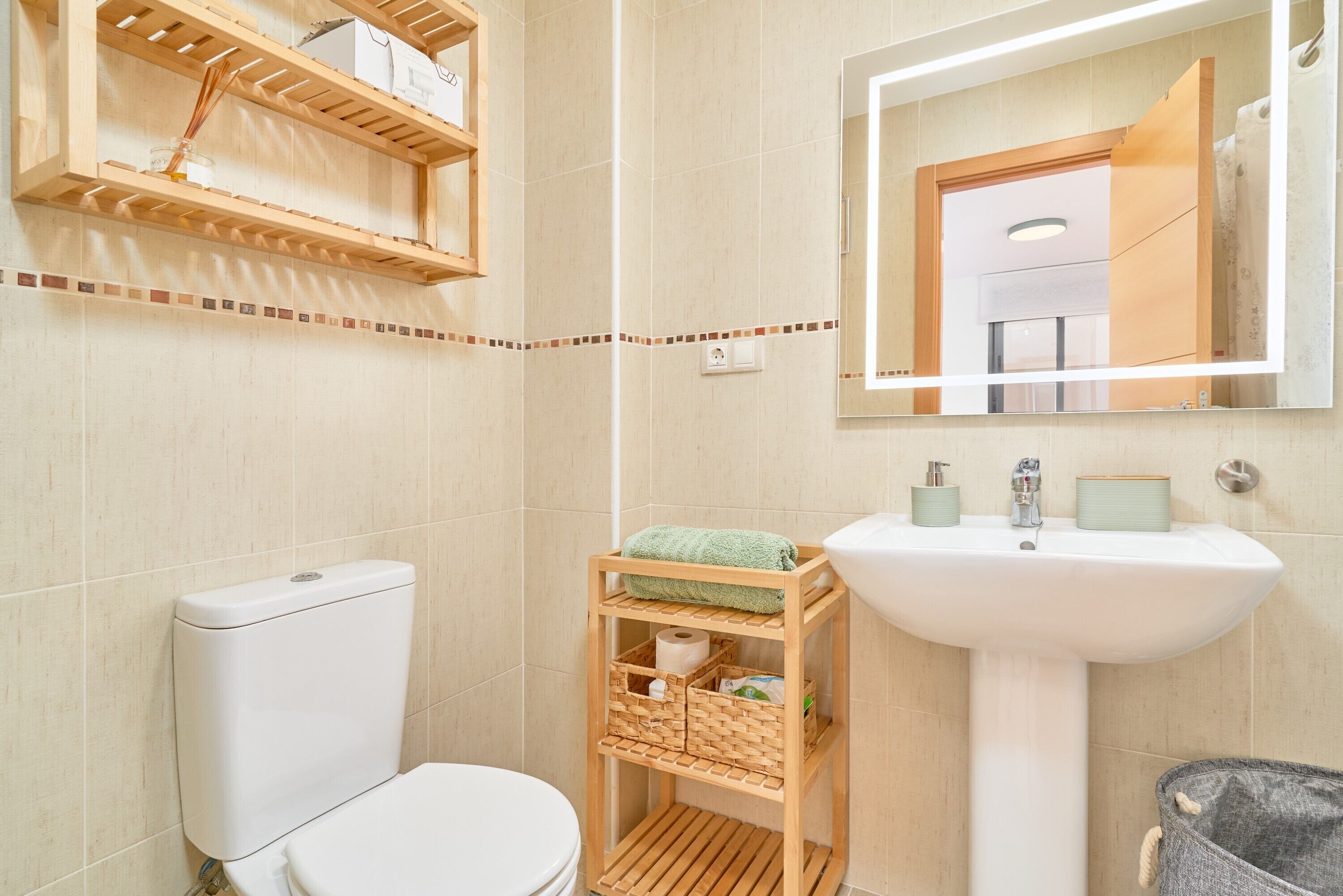 A bathroom with a toilet, a sink, a mirror, and wooden shelves with toiletries.