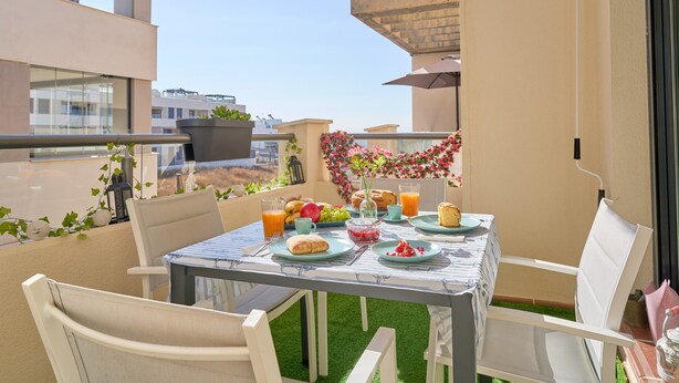 A balcony with a table set for breakfast, outdoor seating, and a view of the cityscape. - 2-Bedroom Penthouse with Sea Views, Wi-Fi, and Air Conditioning (Vélez-Málaga)