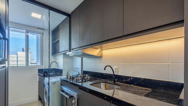 Une cuisine moderne équipée d’une cuisinière à gaz, d’un évier en acier inoxydable et d’une fenêtre donnant sur un paysage urbain.
