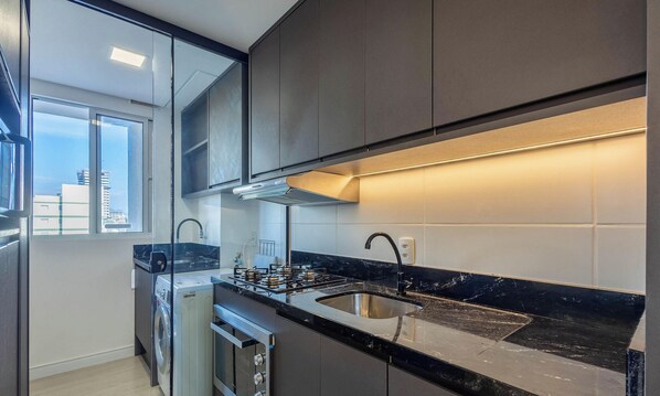 Una cocina moderna con estufa a gas, pileta de acero inoxidable y ventana con vista a la ciudad.