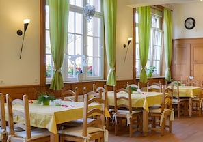 A dining area with wooden tables and chairs, green curtains, and a clock on the wall. - Room 'Christophorus' with Shared Terrace, Shared Garden and Wi-Fi (Forbach)