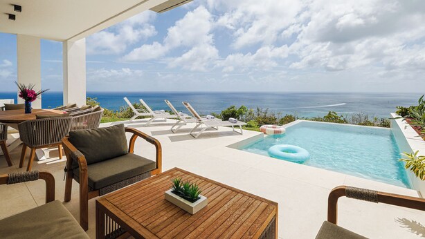 A pool area with lounge chairs, a table, and a view of the ocean. - Villa Turquoise Heaven (Sint Maarten)