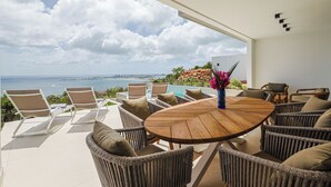 A sunlit outdoor seating area with wicker furniture, a wooden table, and a view of the ocean. - Villa Turquoise Heaven (Sint Maarten)