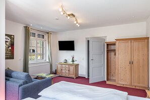 Ein Schlafzimmer mit Bett, Kleiderschrank, Fernseher, einem Fenster mit Vorhängen und einer Deckenleuchte.