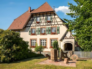 Ein traditionelles Fachwerkhäuschen mit steilem Dach, mehreren Fenstern mit Fensterläden und einem Steineingang.