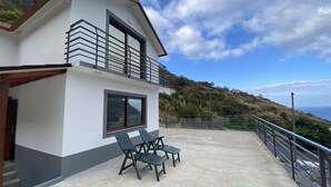 Une maison à deux étages avec un balcon, une terrasse en béton et une vue sur la mer.