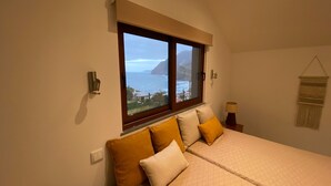 Une chambre avec un grand lit, une fenêtre donnant sur la mer et une lampe fixée au mur.