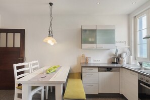 A compact kitchen with white cabinetry, a dining table, a bench, and a hanging light fixture.