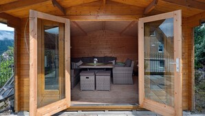 A wooden cabin with a glass door, a sofa, a table, and a bench.