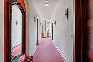 Un pasillo con alfombra roja, puertas de madera y un espejo grande a la izquierda.