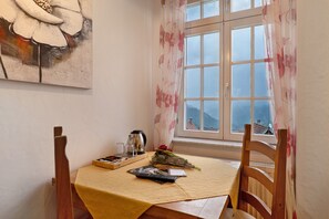 Un coin repas avec une table dressée pour deux personnes, un tableau accroché au mur et une fenêtre donnant sur un beau paysage.