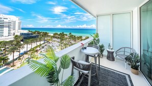 Un balcón con vistas a la playa y al océano, una mesita, dos sillas y plantas en macetas.