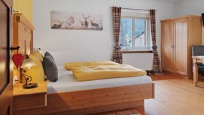 Een slaapkamer met een bed, nachtkastje, lamp, raam met gordijnen, radiator en een houten garderobekast.