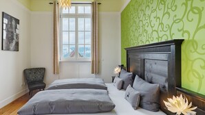 Quarto com cama grande, uma cadeira, janela com cortinas, lareira e parede com padrão verde.