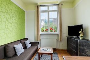 A living room with a sofa, a coffee table, a television on a stand, and a window with curtains.