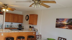 A kitchen with wooden cabinets, a marble countertop, and a dining area with a glass table and wooden chairs. -  across from Charley Young  beach #2 (Kihei)