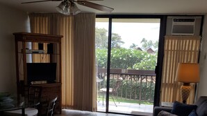 A living room with a ceiling fan, a TV on a wooden stand, a sofa with patterned cushions, a dining table with chairs, and a view through a glass door to the outside. -  across from Charley Young  beach #2 (Kihei)