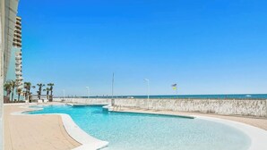 A swimming pool with a curved edge, a beach view, and a flagpole with an American flag. - Beautiful 2B/2B Beach Views & Best Eats | Palmaway (Gulf Shores)