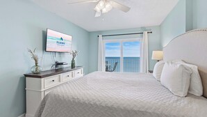 A bedroom with a bed, a ceiling fan, a TV, a dresser, a window with a view, and a chair. - Beautiful 2B/2B Beach Views & Best Eats | Palmaway (Gulf Shores)
