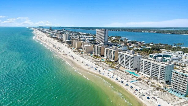 An aerial view of a coastal city with a long beachfront, high-rise hotels, and a clear blue sea. - Beautiful 2B/2B Beach Views & Best Eats | Palmaway (Gulf Shores)