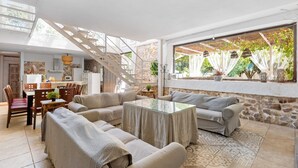 A spacious living area with a glass coffee table, sofas, a dining table, and a staircase leading to an upper level.