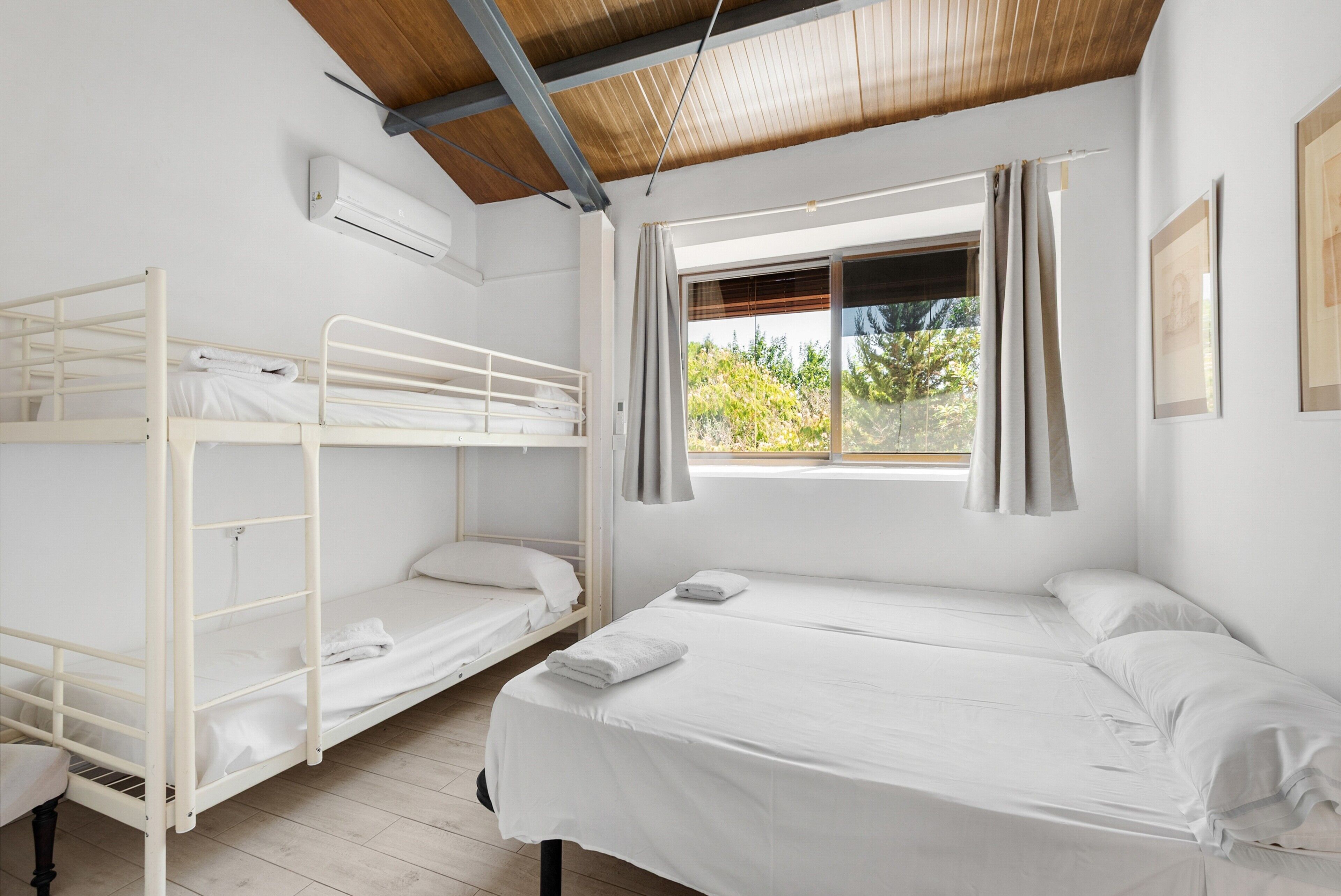 A dormitory room with bunk beds, a window with curtains, and an air conditioning unit.