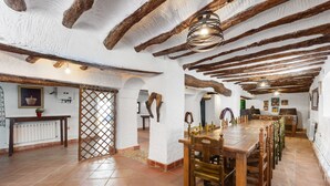 A rustic interior with exposed wooden beams, a long wooden dining table, and a tiled floor.