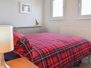 Una camera da letto con un letto, un comodino, una lampada, una cassettiera, una finestra e un termosifone.