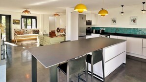 A modern kitchen with a central island, pendant lighting, and a dining area with a sofa and chairs.