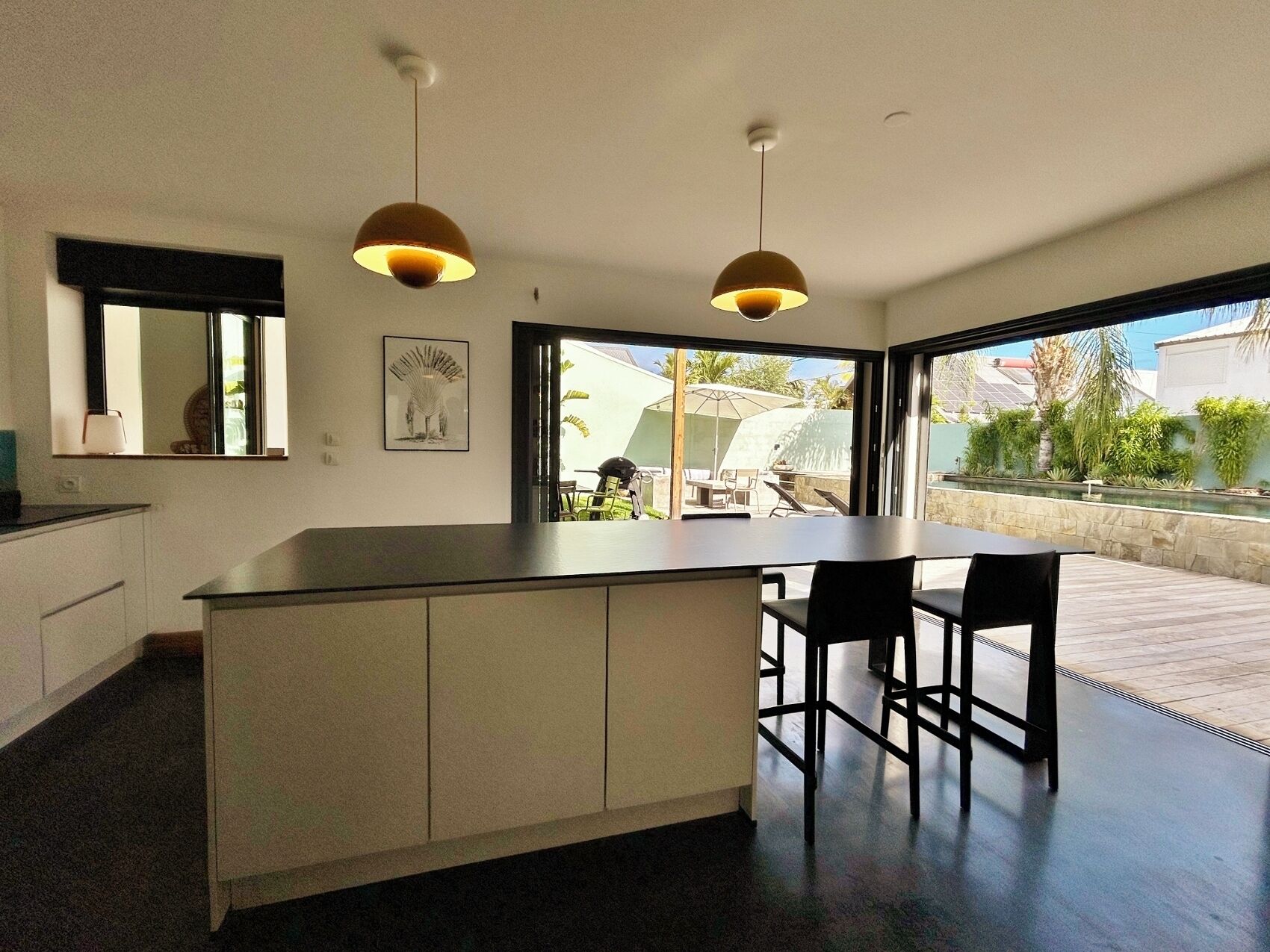 A modern kitchen with a central island, two pendant lights, and a view of the outdoor patio.