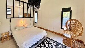 A bedroom with a bed, a hanging light fixture, a chair, and a window.