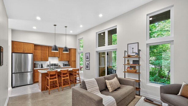 A modern kitchen with wooden cabinets, a stainless steel refrigerator, and a dining area with a bar stool. - 500 House - Unit A 1 Bedroom Townhouse (Mequon)