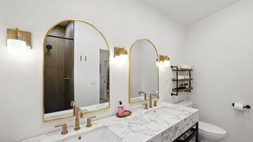 A modern bathroom with a white marble sink, gold fixtures, and a large mirror with gold frames.