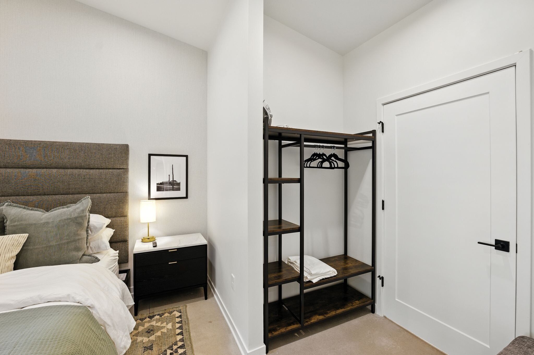 A bedroom with a bed, bedside table, lamp, and a wardrobe with shelves.