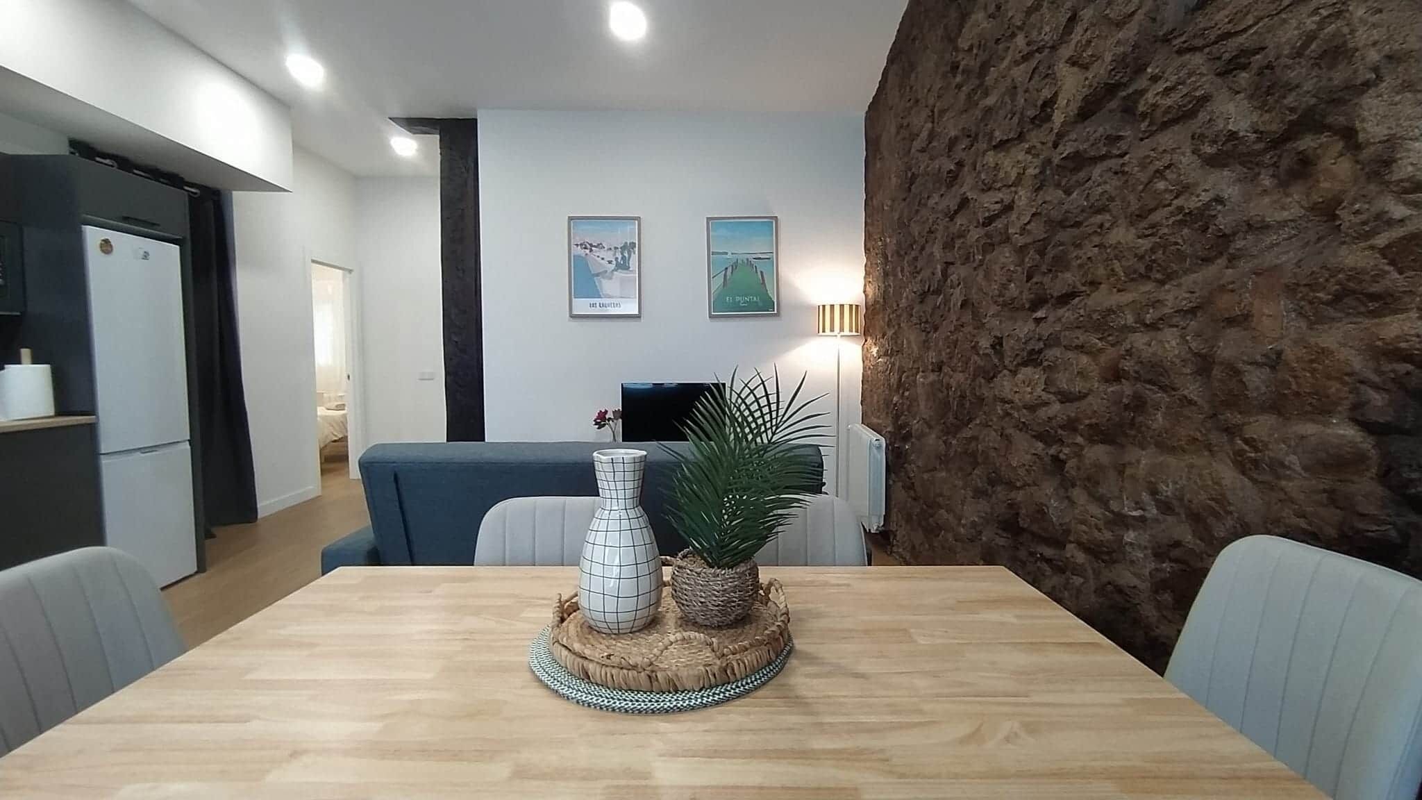 A dining area with a wooden table, chairs, a vase, and a plant centerpiece.