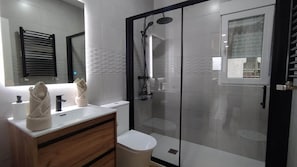 A modern bathroom with a glass-enclosed shower, a wooden vanity, and a toilet.