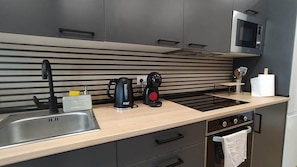A modern kitchen with a stainless steel sink, a kettle, a coffee maker, and a microwave.
