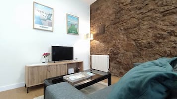 En stue med en stenvæg, et fladskærms-tv på et træbord, en sofa og et sofabord med en bog.