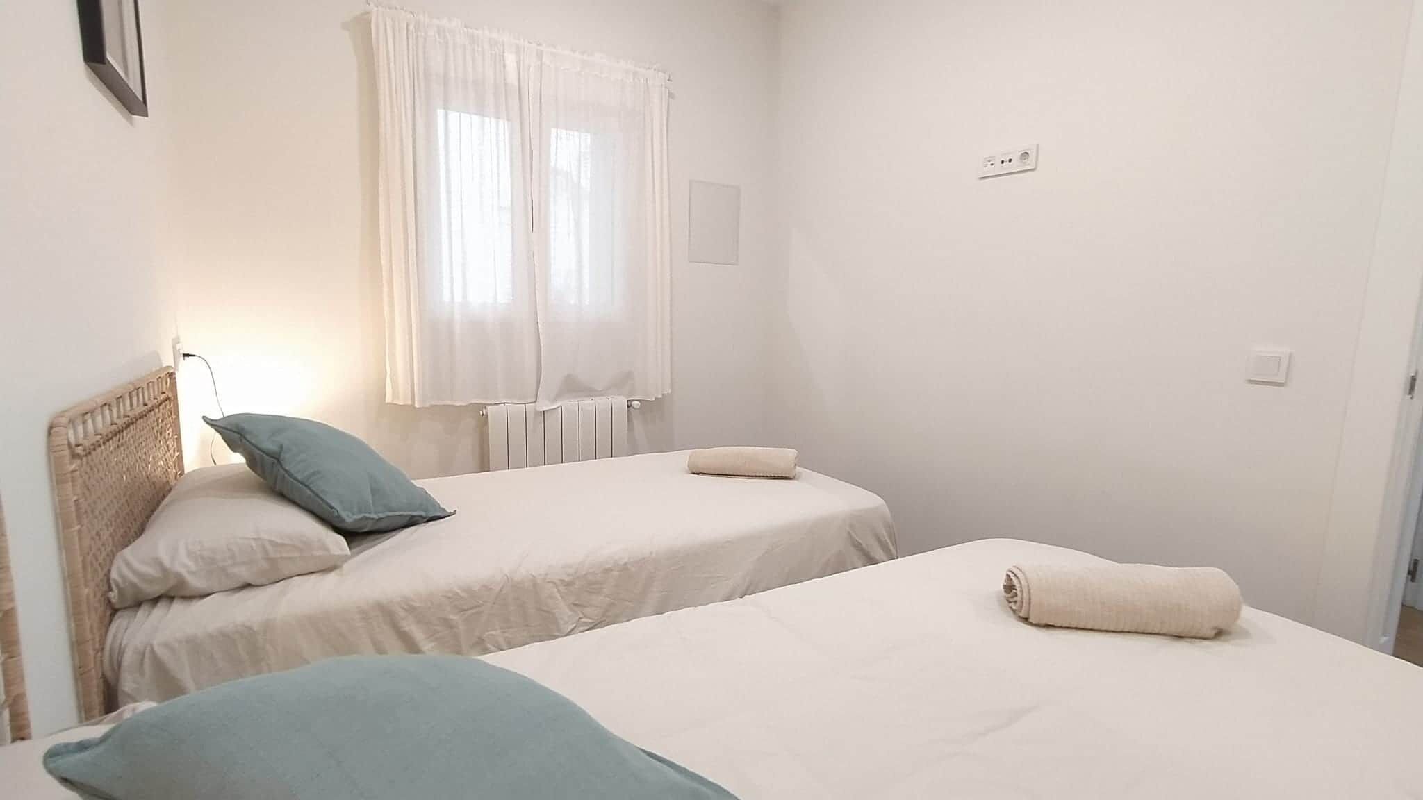 A simple, clean room with two beds, a window with curtains, and a radiator.
