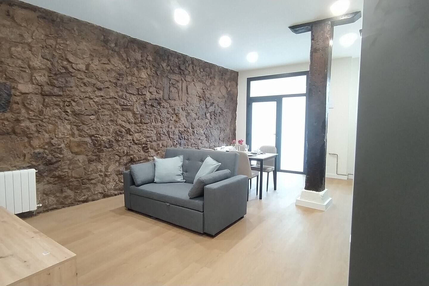 A living room with a stone wall, a grey sofa, a dining table, and a large window.