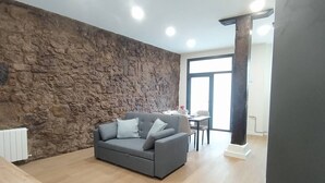 Un salon avec un mur en pierre, un canapé gris, une table à manger et une grande fenêtre.
