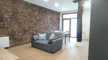 A living room with a stone wall, a grey sofa, a dining table, and a large window.